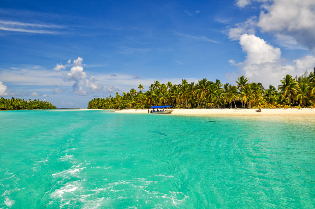 A view of the one-foot island off of Aitutaki with a boat docked on short and an empty white sandy beach.